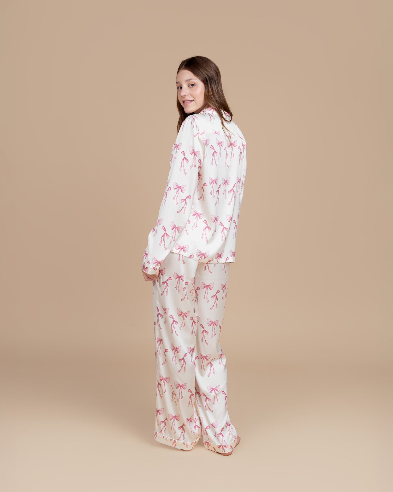 Teen model wearing Dream Queen Co. Sleep Cute Long sleeve satin set in Coquette Code pink Bow Print