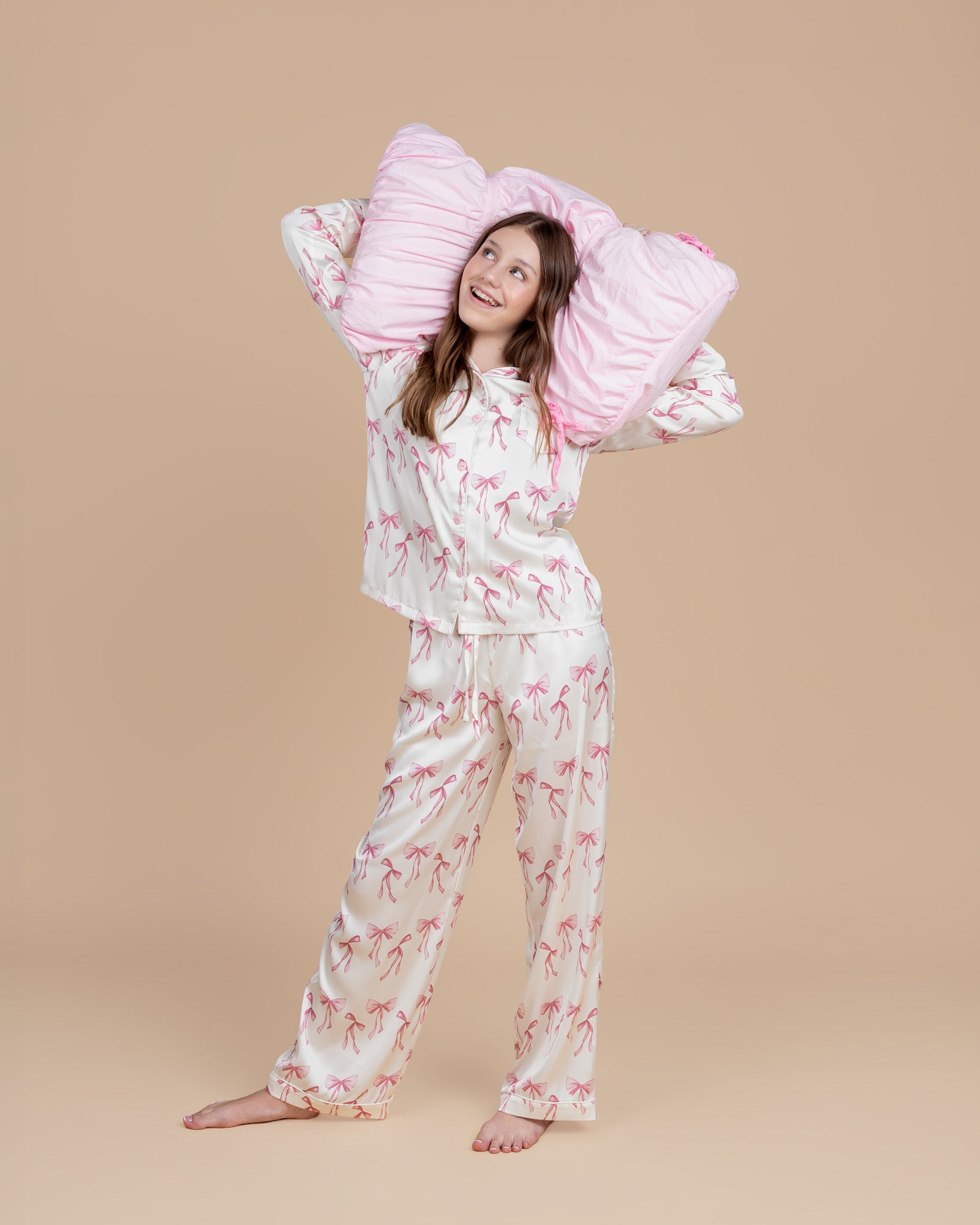 Teen model wearing Dream Queen Co. Sleep Cute Long sleeve satin PJ set in Coquette Code pink Bow Print