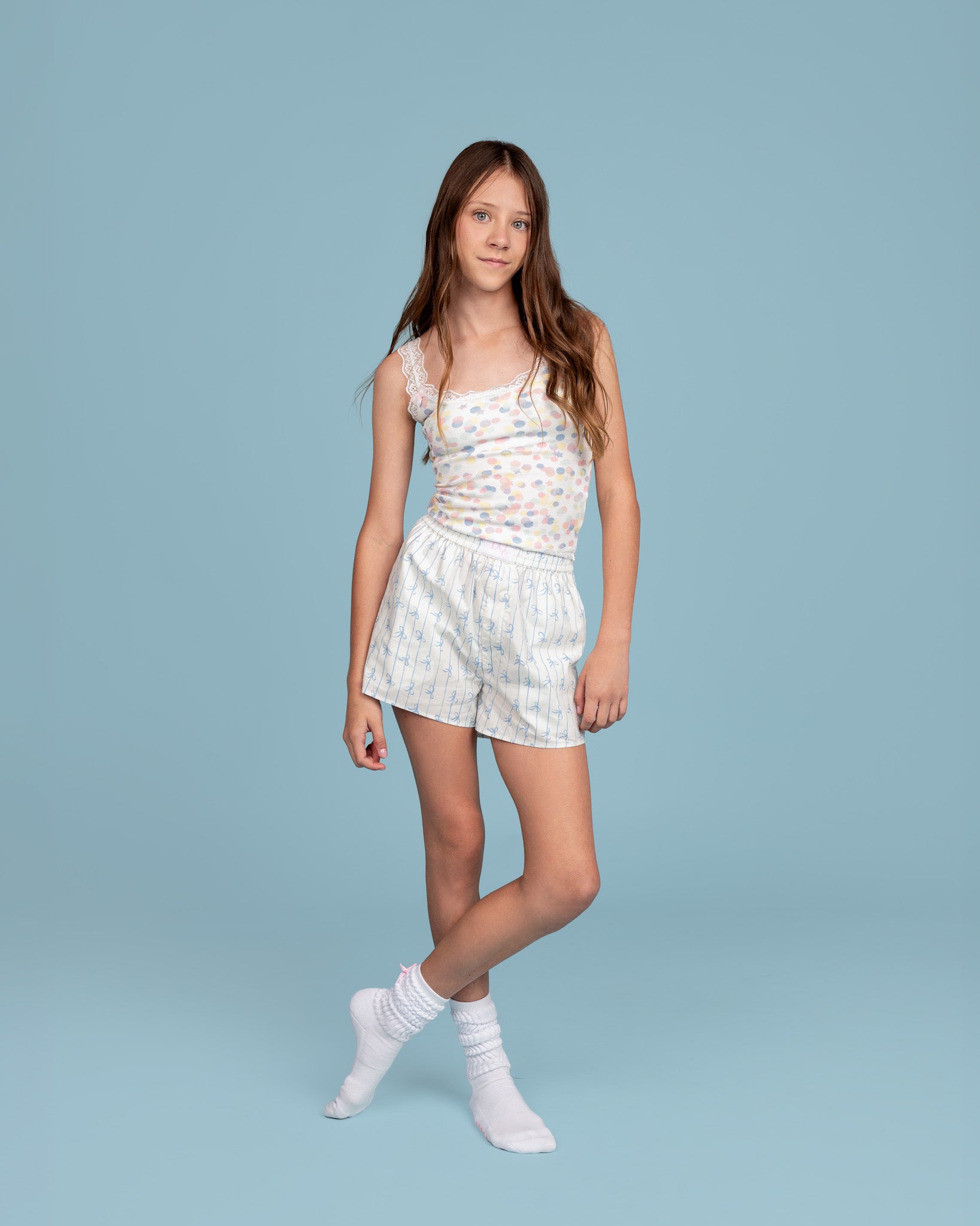Tween model wearing Dream Queen Co. Love Lines boxer short  in blue bow stripe, confetti print dreamley waffle top, and white grip socks