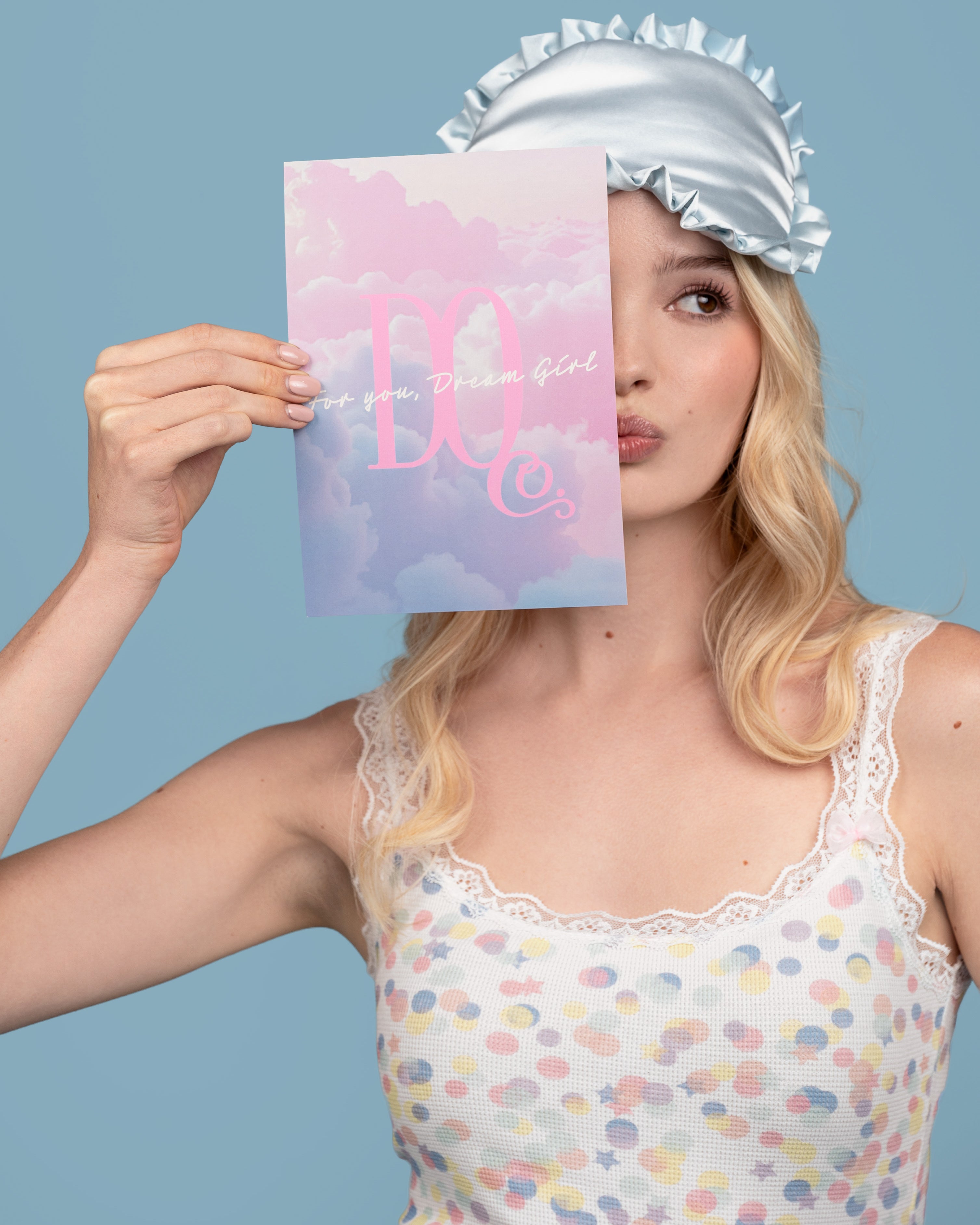 Model in confetti crush pastel print top holding a Dream Queen Gift Card with a blue and pink design 